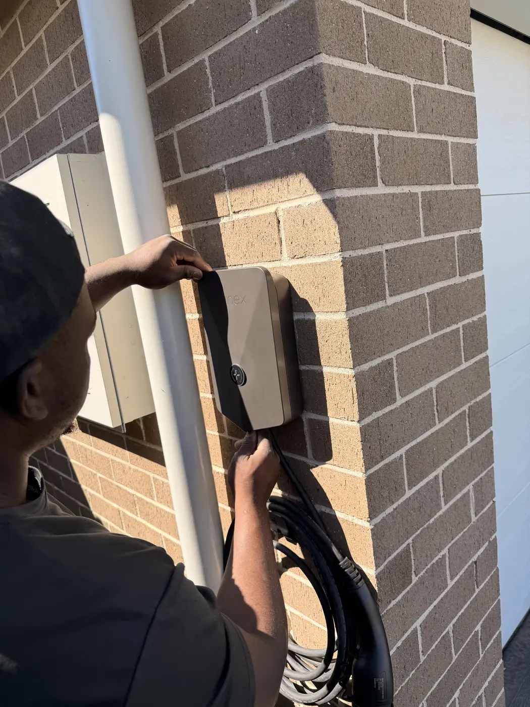 Mutsa mounting an EV charger on a brick home